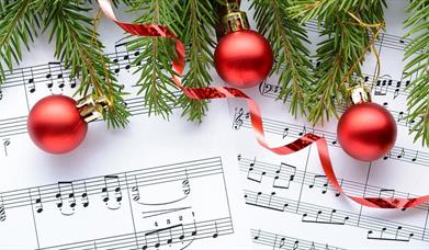 Red Christmas baubles and the branches of a Christmas tree overlaid on a sheet of music