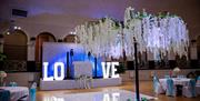 Interior of a wedding venue with the word Love spelt out on the stage and with an artificial white tree in the middle of the floor surrounded by dinin