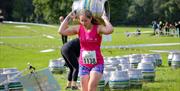 A female sports competitor in pink top and blue shorts running with a heavy beer barrel on her shoulders