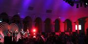 A band on stage in front of a full crowd under atmospheric lighting in a ballroom