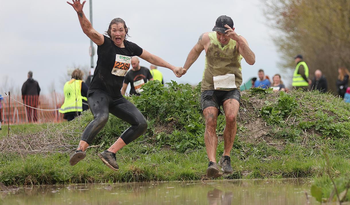 Two competitors in an endurance race jump together above a water pit