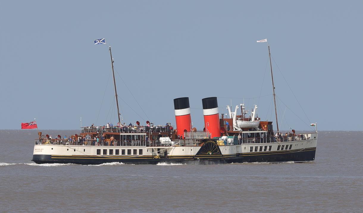 A paddle steamer out at sea with passengers crammed onto the deck