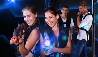 Two girls firing laser guns with two males in the background