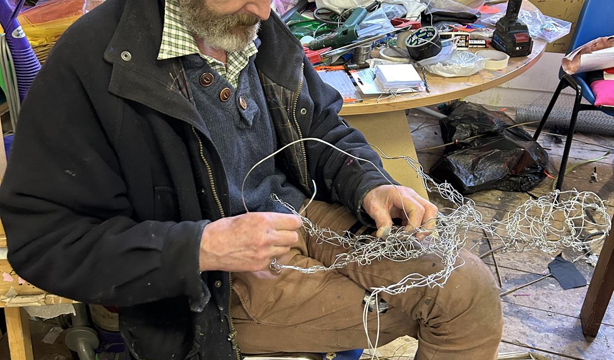 Man sat on chair working with wire creating a fairy sculpture