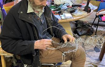 Man sat on chair working with wire creating a fairy sculpture