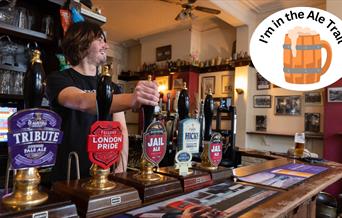 A barman pulling a pint in a pub over-stamped with an I'm in the ale trail logo