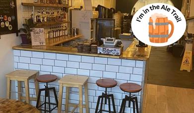 An empty bar counter with white tiles and five assorted stools in front of it