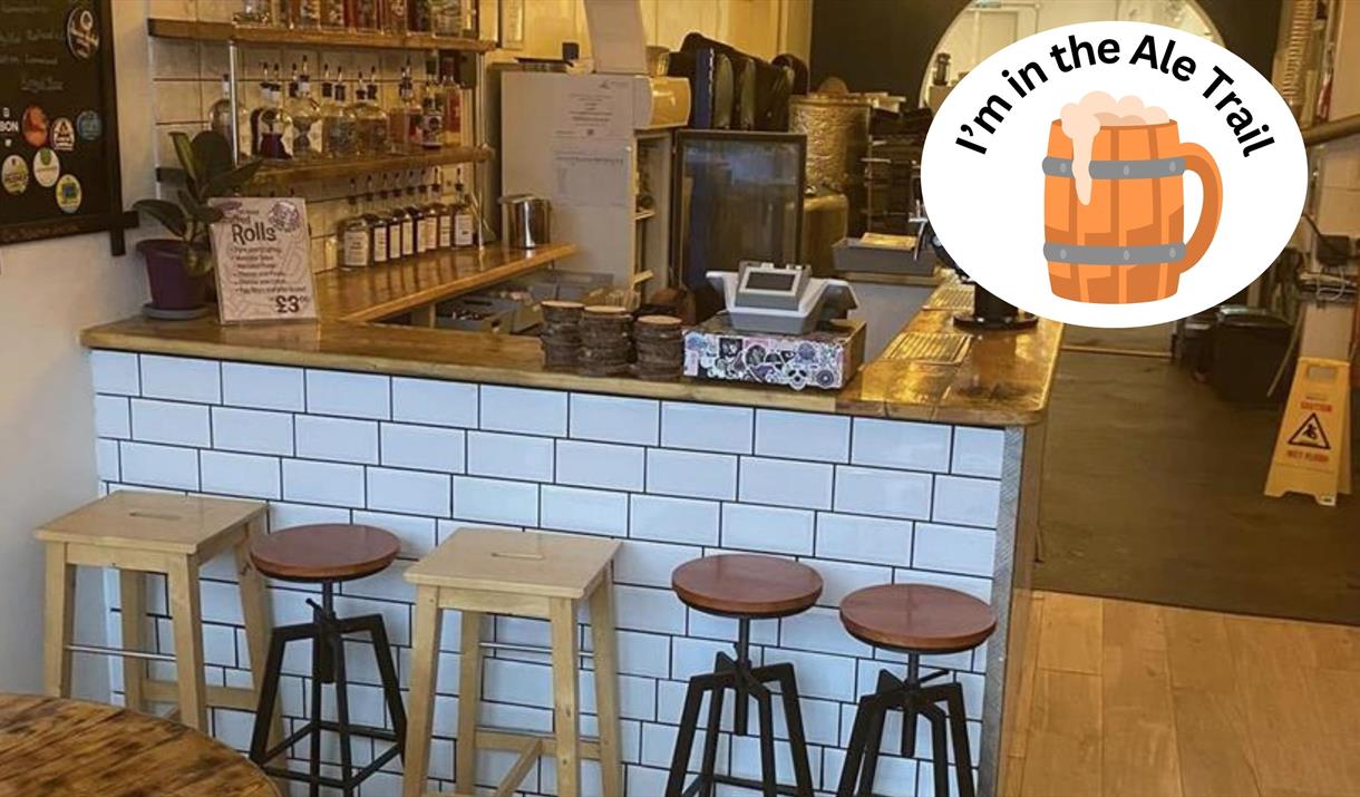 An empty bar counter with white tiles and five assorted stools in front of it