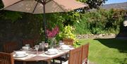 A wooden garden table with parasol set for a meal on a sunny day with lawn in the background