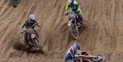 Two motorcyclists have to avoid a fallen rider as they come down a steep sand dune in a beach race