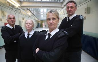 Four prison guards standing in the middle of a prison wing