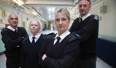 Four prison guards standing in the middle of a prison wing