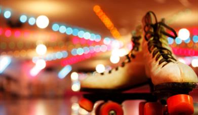 White roller boots with red wheels on a wooden floor.
Bright disco lights in the background.