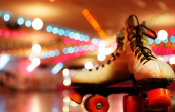 White roller boots with red wheels on a wooden floor.
Bright disco lights in the background.