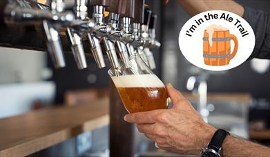 A hand tilting a glass and filling it with beer at the pump