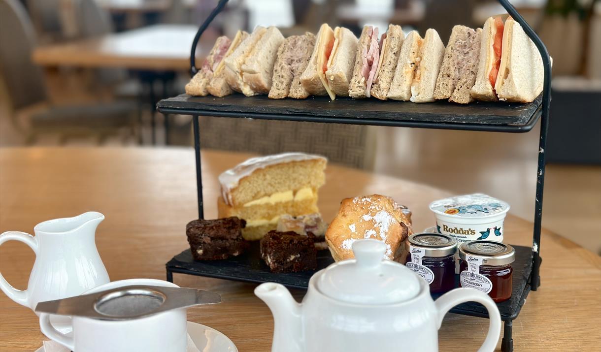 Traditional afternoon tea with pot of tea and cake stand with cakes and sandwiches