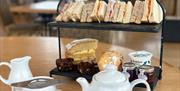 Traditional afternoon tea with pot of tea and cake stand with cakes and sandwiches