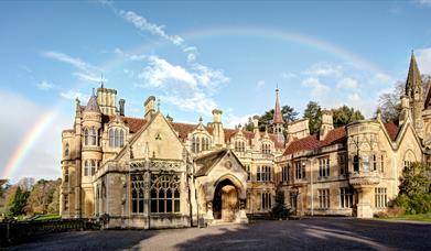 Exterior view of a large turreted mansion with a rainbow above