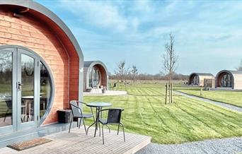Entrance to a luxury glamping pod with seats on the decking and other pods in the background