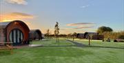 Two curved glamping pods in a field at sunset