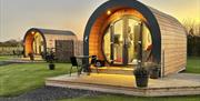 Illuminated exteriors of two glamping pods at sunset