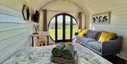 Interior of a luxury wooden glamping pod with towels on a double bed, and a large sofa with yellow  cushions