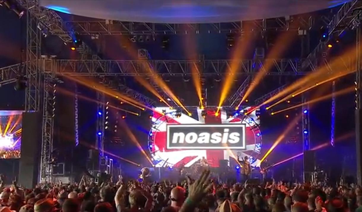A crowd of people with hands raised facing Noasis