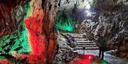 Inside of a cave leading to some stone steps illuminated with red and green lighting