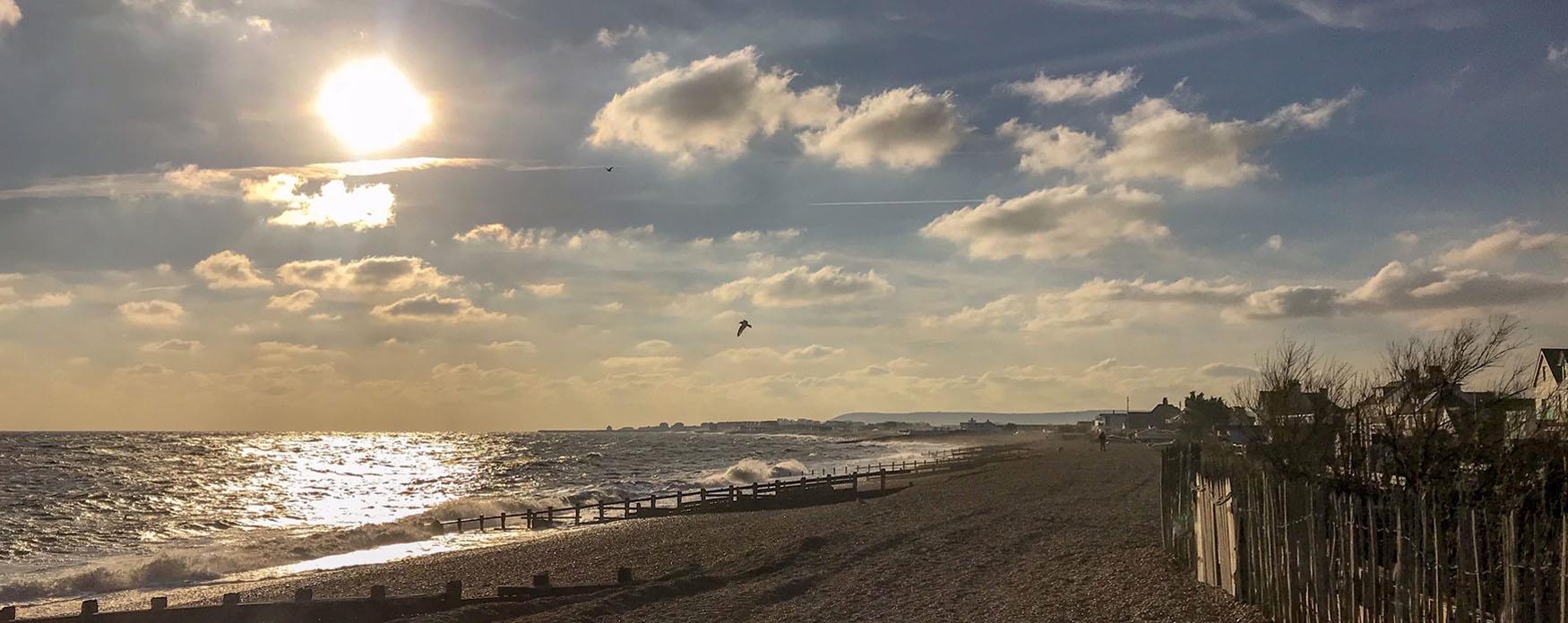 the sun shimmering on the waves from a pebble beach