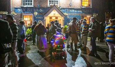 A group of people hanging outside a pub at night, ready for a bonfire procession