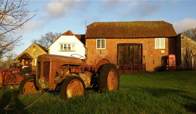 old style tractor in front of farmhouse with a red telephone box in front