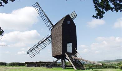 a windmill sitting on grass, looking out towards the hills