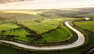 winding river with green fields and dappled sunshine