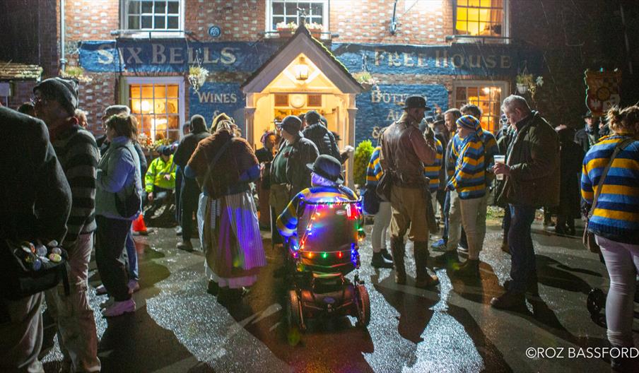 A group of people hanging outside a pub at night, ready for a bonfire procession
