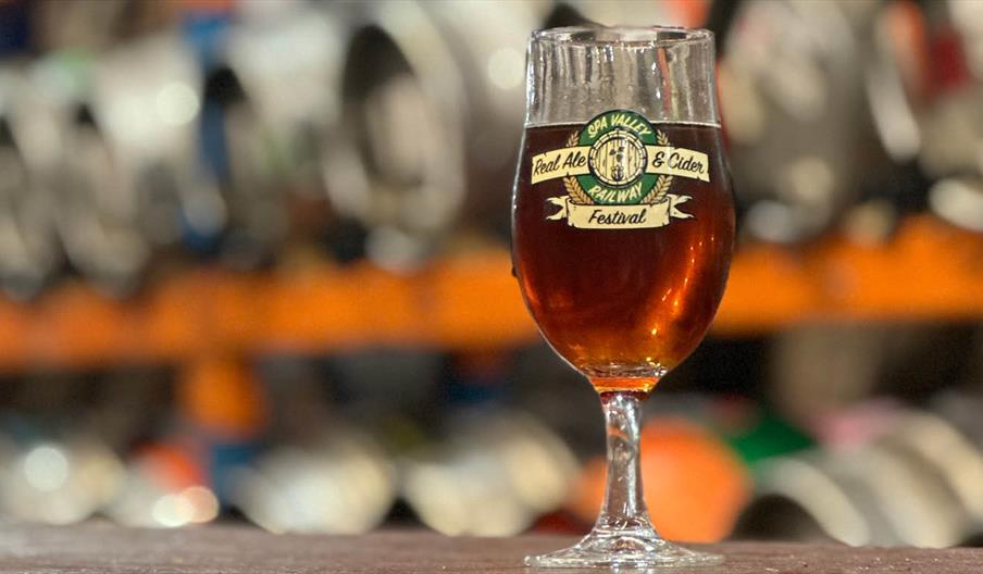 A glass of ale with kegs in the background
