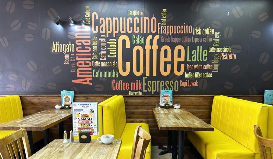 Interior of Aroma Café with yellow booth seating and large coffee-themed wall mural featuring words like cappuccino, espresso and latte