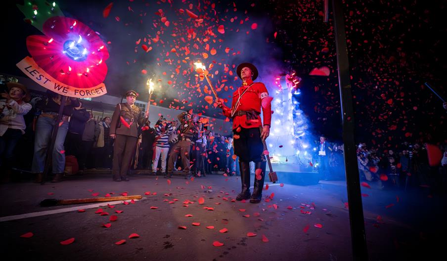 Remembrance-themed display at the East Hoathly Carnival and Bonfire celebrations, featuring a large illuminated poppy, torchbearers and falling red pe