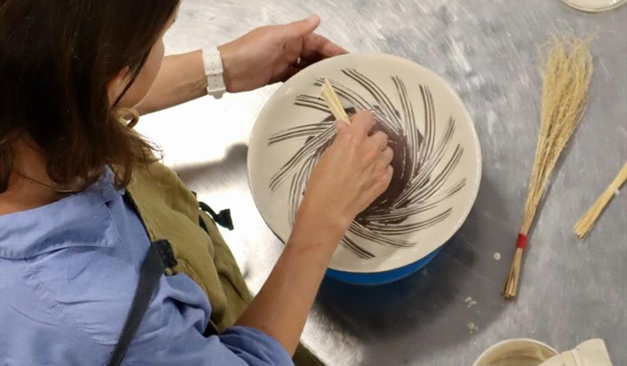 Image of a lady painting a plate with the Hakeme Brushwork