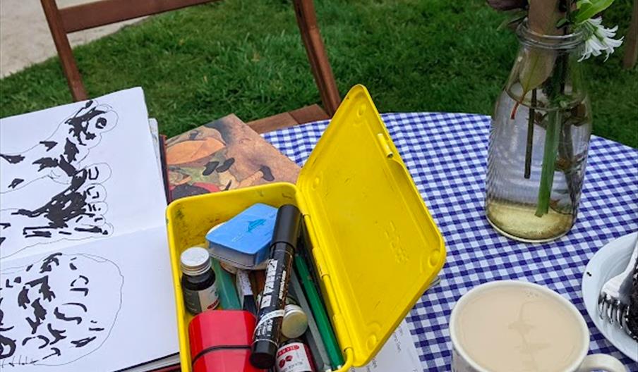 an outside table with craft supplies and a sketchbook on top