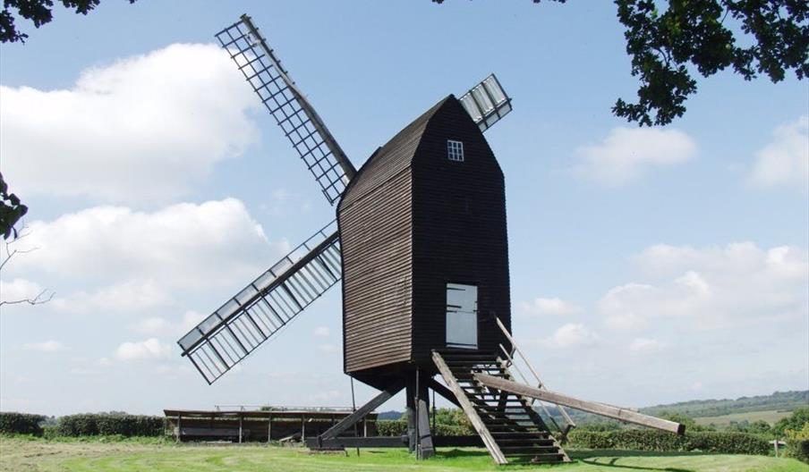 a windmill sitting on grass, looking out towards the hills