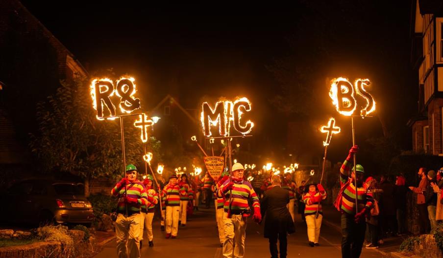 Torchlit procession at the Rotherfield Bonfire celebrations, with participants carrying flaming society signs and torches through the village streets