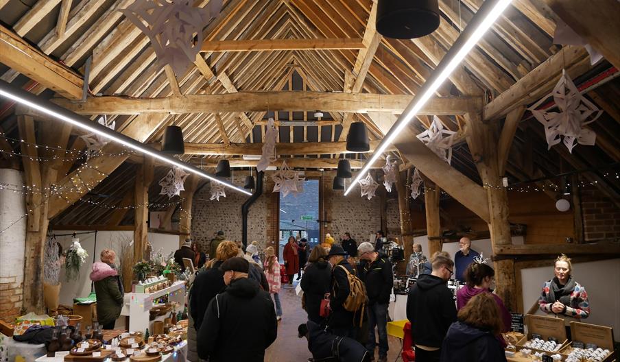 A Christmas market held in a barn, with people shopping at the various stalls