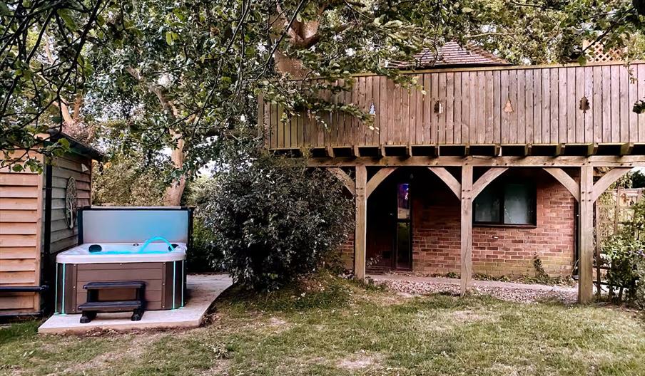 Treehouse-style countryside accommodation featuring a private hot tub, timber balcony and sheltered outdoor space beneath mature trees.