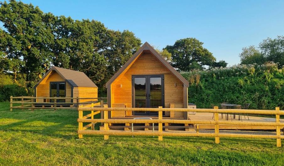 Two wooden cabins in a field with trees in the background