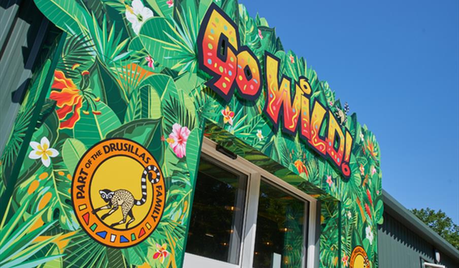 Entrance to Go Wild! in Heathfield, decorated with vibrant tropical artwork and Drusillas Family Theme Park branding.