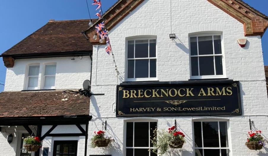 An image of the Brecknock Arms. It is painted white with a black sign in the centre of the building.