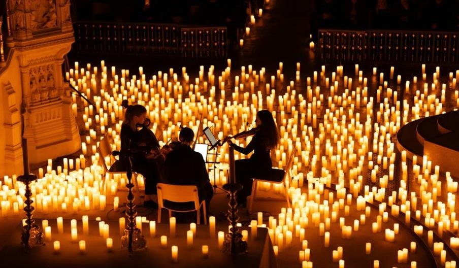 a trio of classical musicians, surrounding by candles lit up on the floor