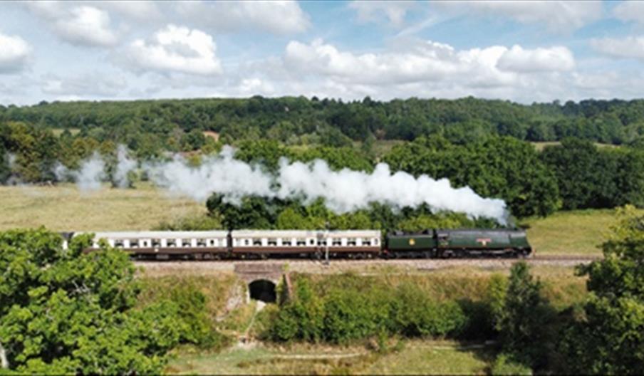 A vintage steam train driving on a railway bridge through the High Weald countryside