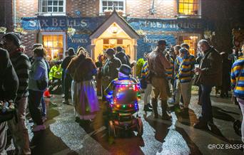 A group of people hanging outside a pub at night, ready for a bonfire procession