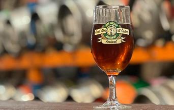 A glass of ale with kegs in the background